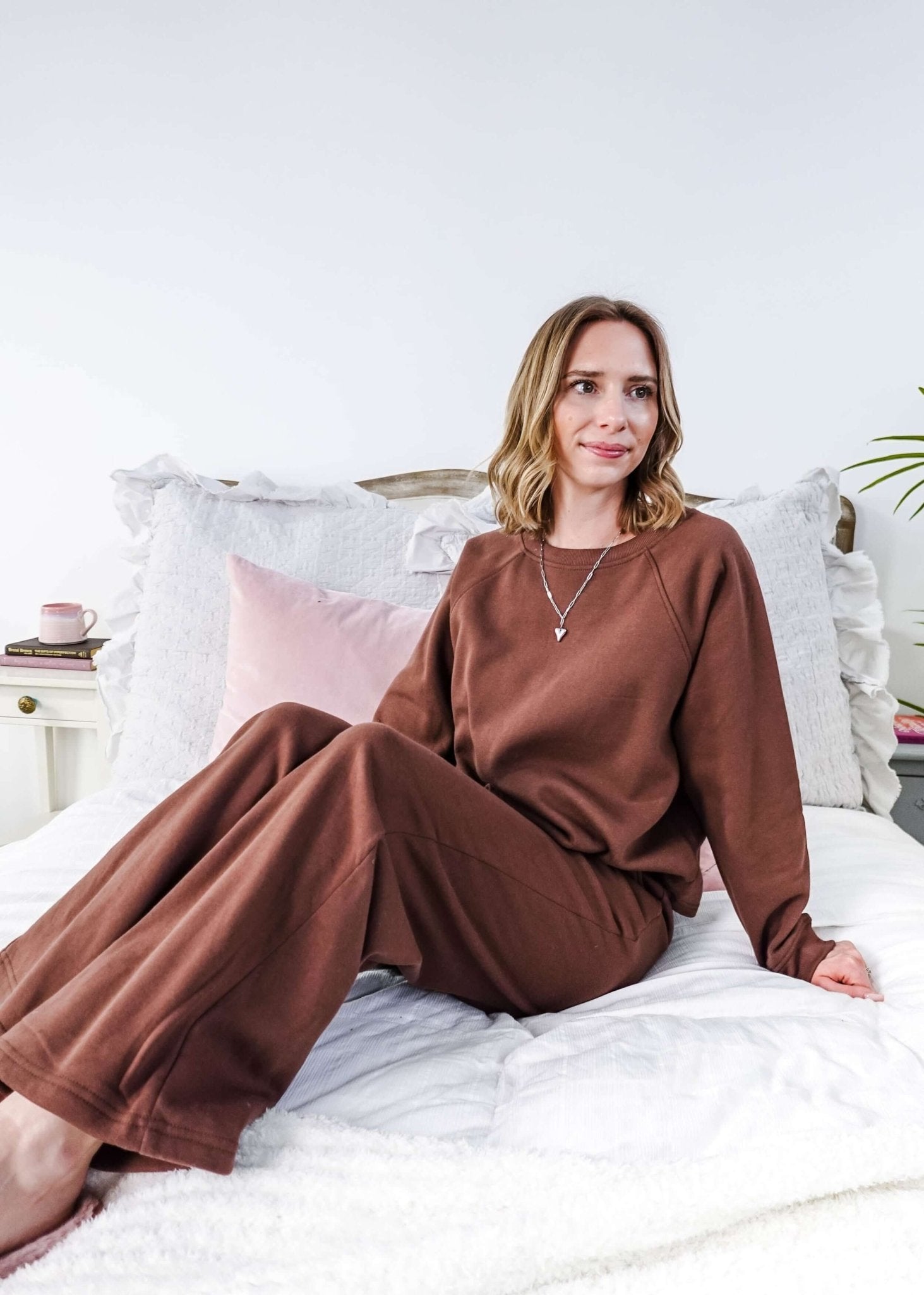 Woman in brown lounge set  sitting on a bed with white bedding