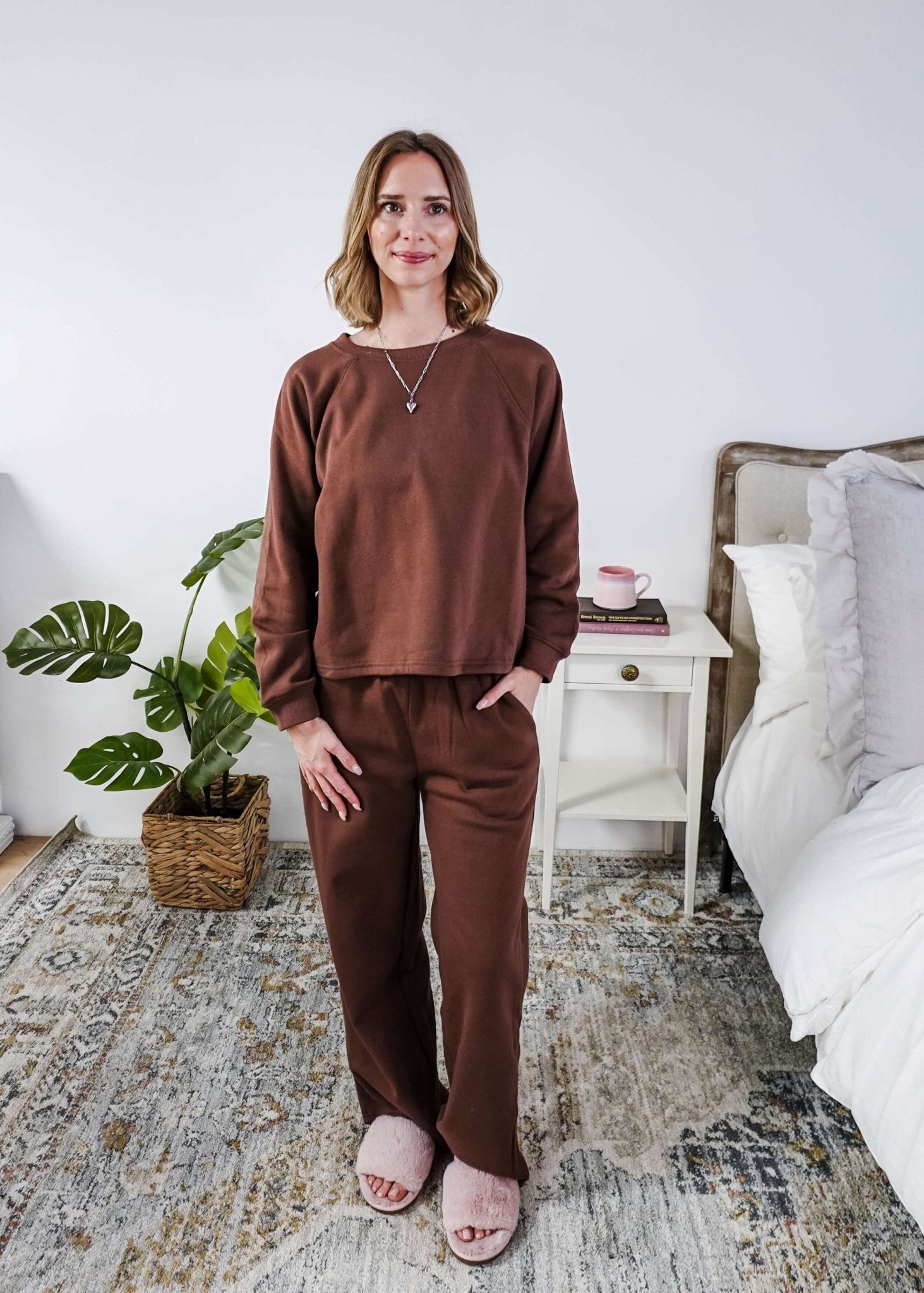 Woman wearing a brown lounge outfit standing in a bedroom.