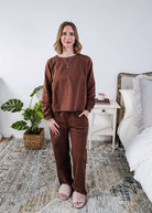 Woman wearing a brown lounge outfit standing in a bedroom.