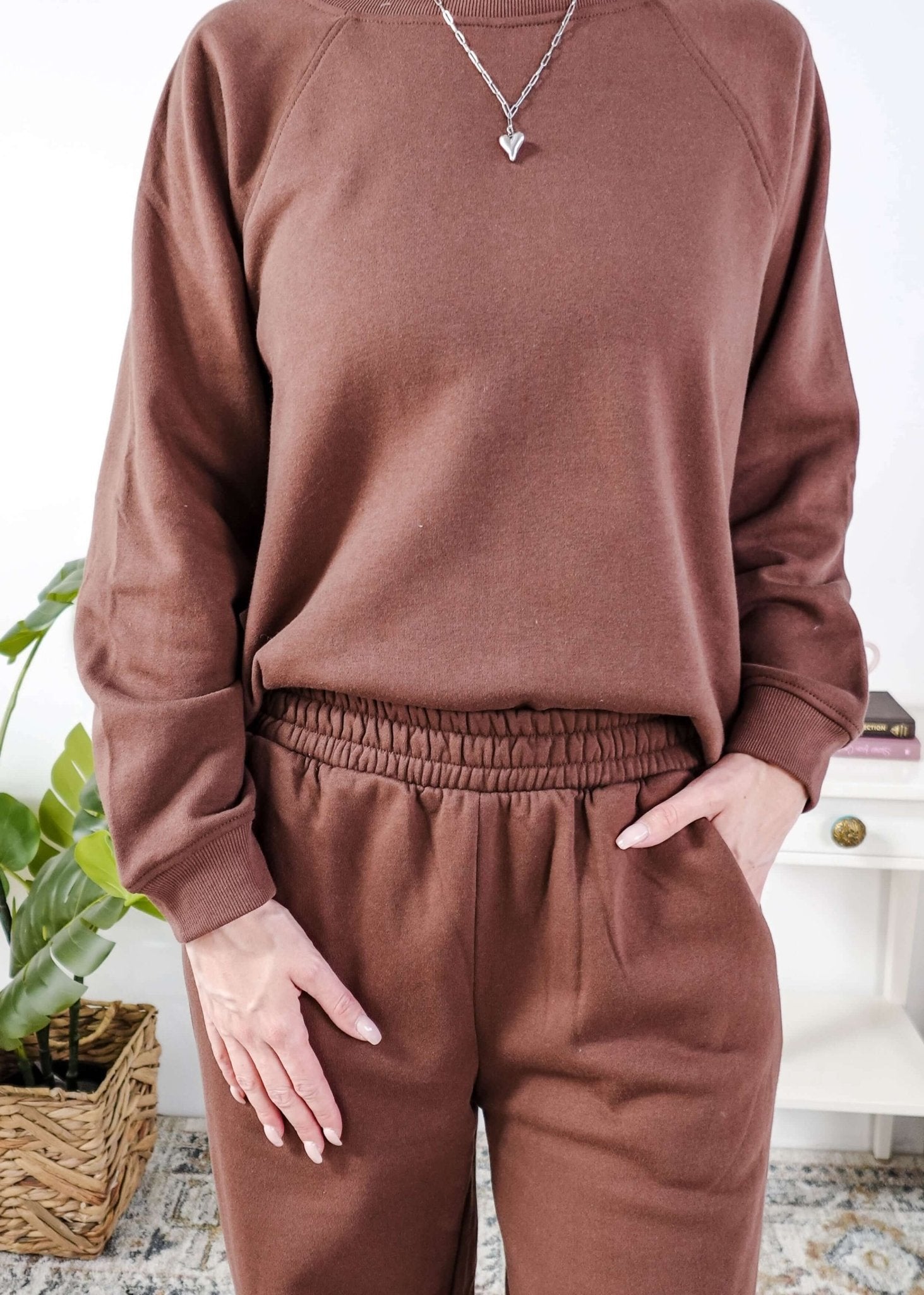 Person wearing a brown sweatshirt and sweat pants with elastic waistband and pants in a home setting.