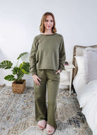 Woman wearing an olive green sweatset standing in a bedroom.