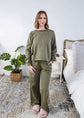 Woman wearing an olive green sweatset standing in a bedroom.