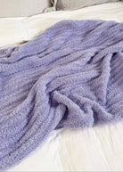 Purple blanket draped over a bed with beige pillows