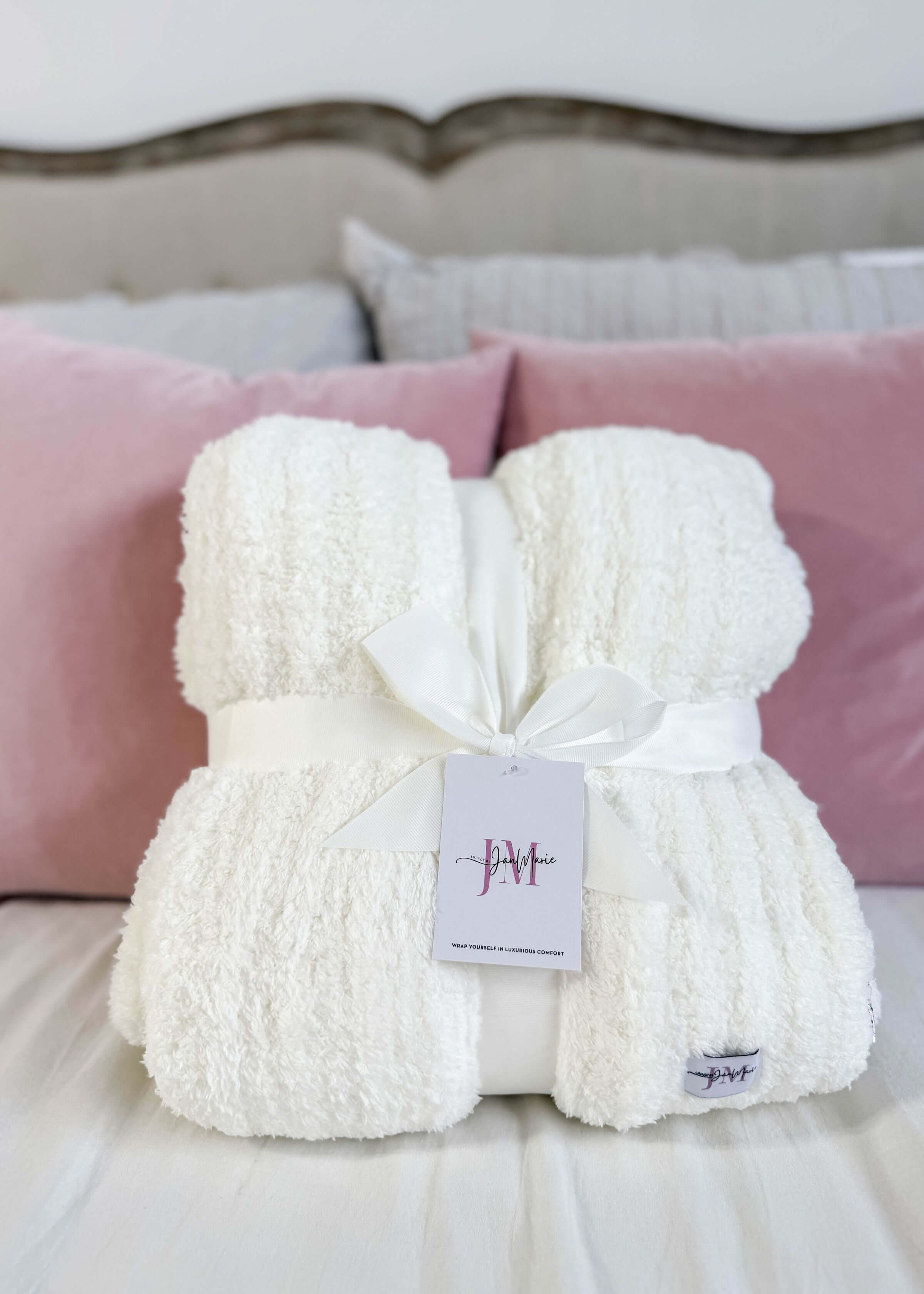 White fluffy blanket with a tag on a bed with pink pillows