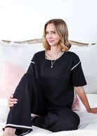 Woman wearing a black outfit with white trim sitting on a bed.