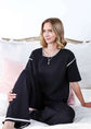 Woman wearing a black outfit with white trim sitting on a bed.