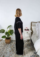 Woman in a black lounge outfit standing in a bedroom with a plant and bed in the background