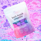 Mermaid Bath Bomb Crumble in a colorful package with fizzling bath water in the background.