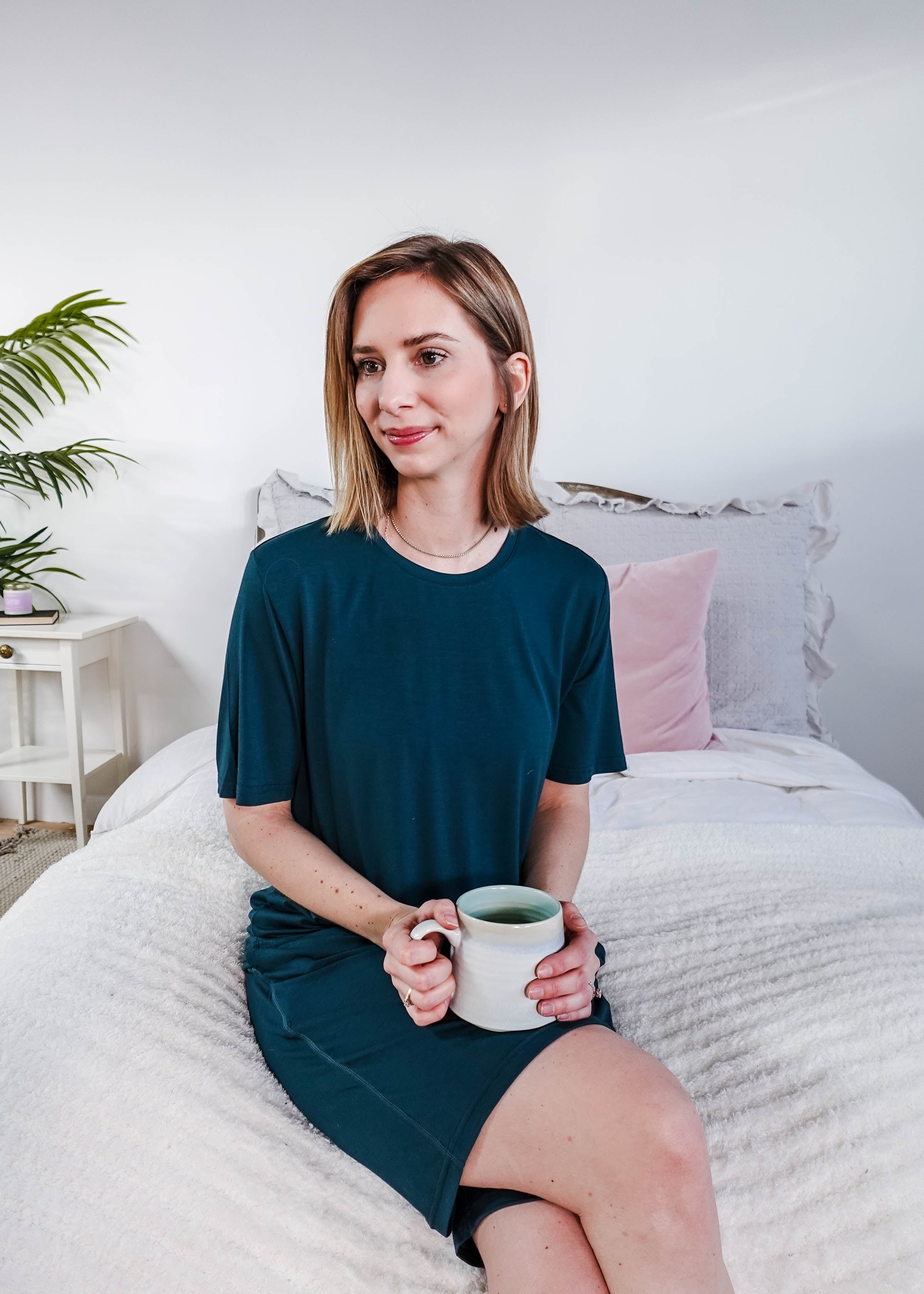 Woman wearing Midnight Teal Unisex Bamboo Sleep Shorts while holding a cup of tea in a cozy bedroom setting.