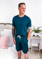 Midnight Teal Unisex Bamboo Sleep Shorts being modeled in a cozy bedroom setting with light decor.