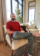 Man sitting comfortably in Mistletoe Print Unisex Bamboo Jogger, enjoying a drink in a cozy living room.