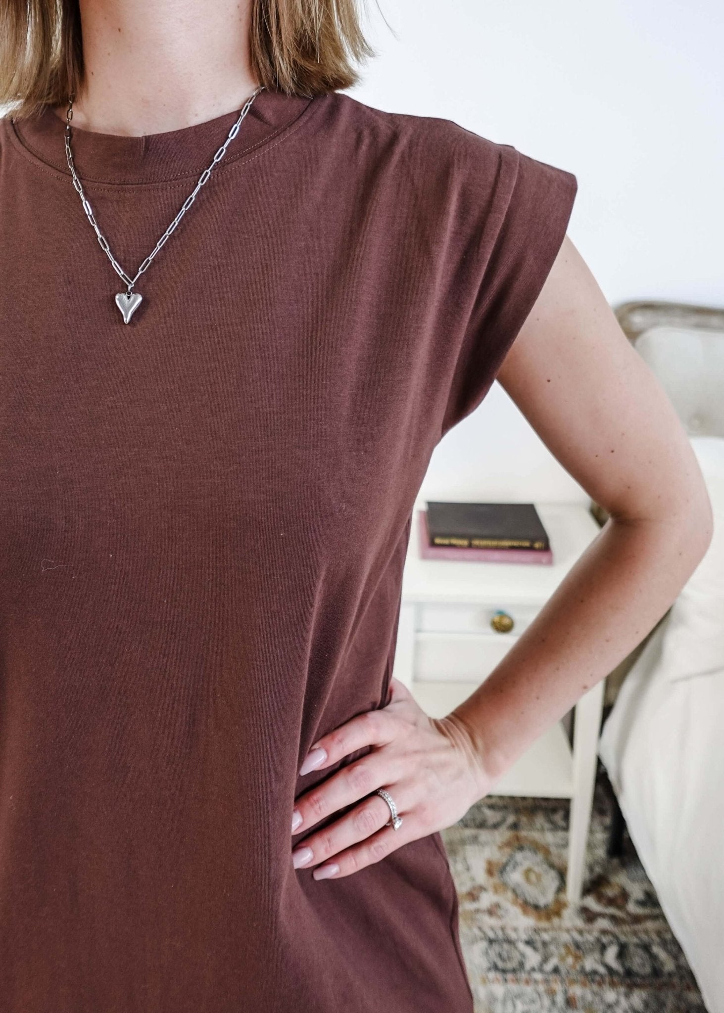 Close up of Woman in a brown midi dress holding a beige handbag in a bedroom setting.