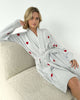 Model wearing the Pomona Fuzzy Yarn Robe Splendid in gray with red hearts, sitting on a plush chair.