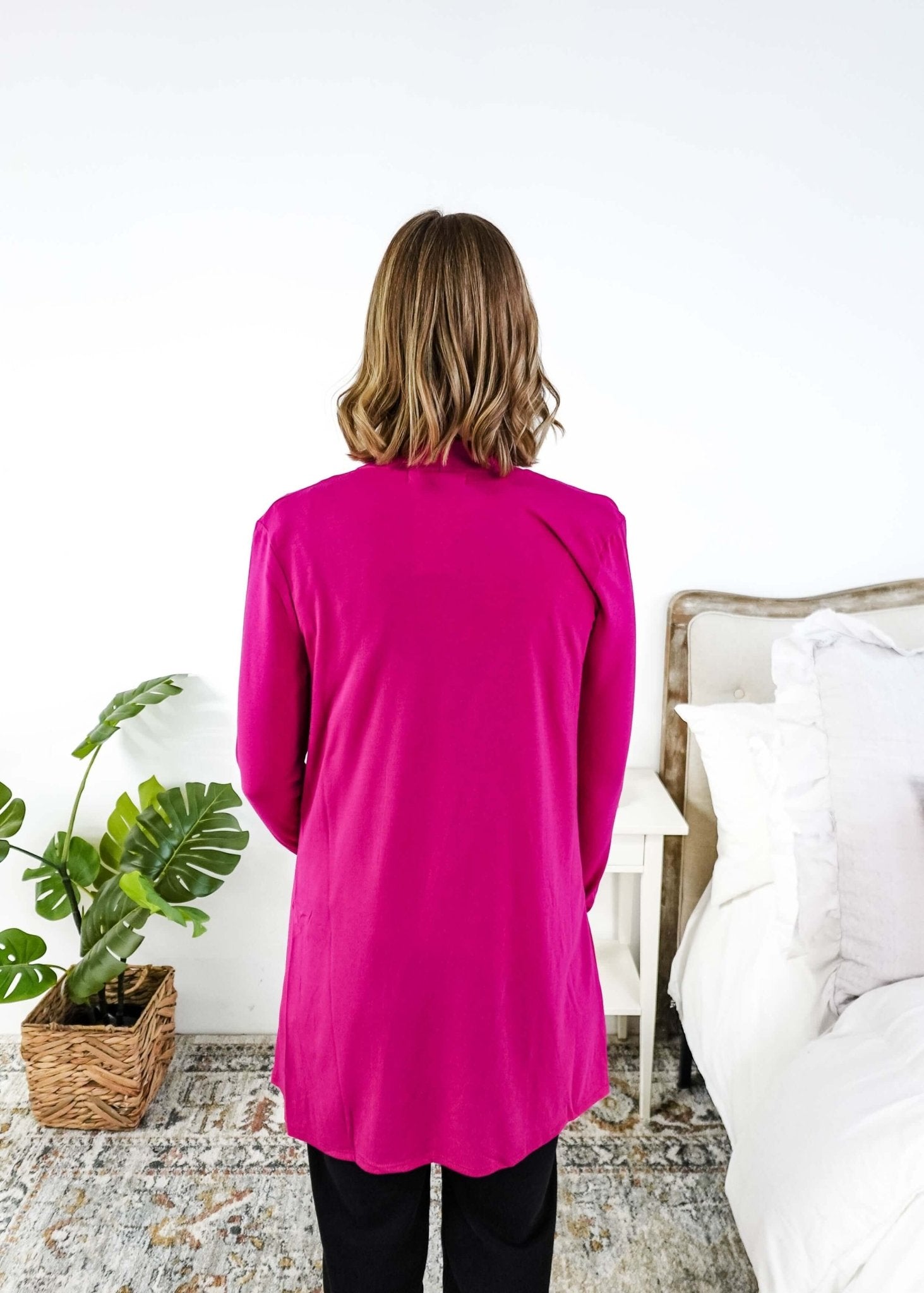 Women wearing a bright pink long-sleeve cardigan in a bedroom setting. Scarlett Ellie Summer Open Lightweight Cardigan | Cloud Nine Pajamas