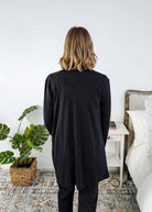 Woman in a black cardigan standing in a room with a plant and a bed in the background Scarlett Ellie Summer Open Lightweight Cardigan | Cloud Nine Pajamas