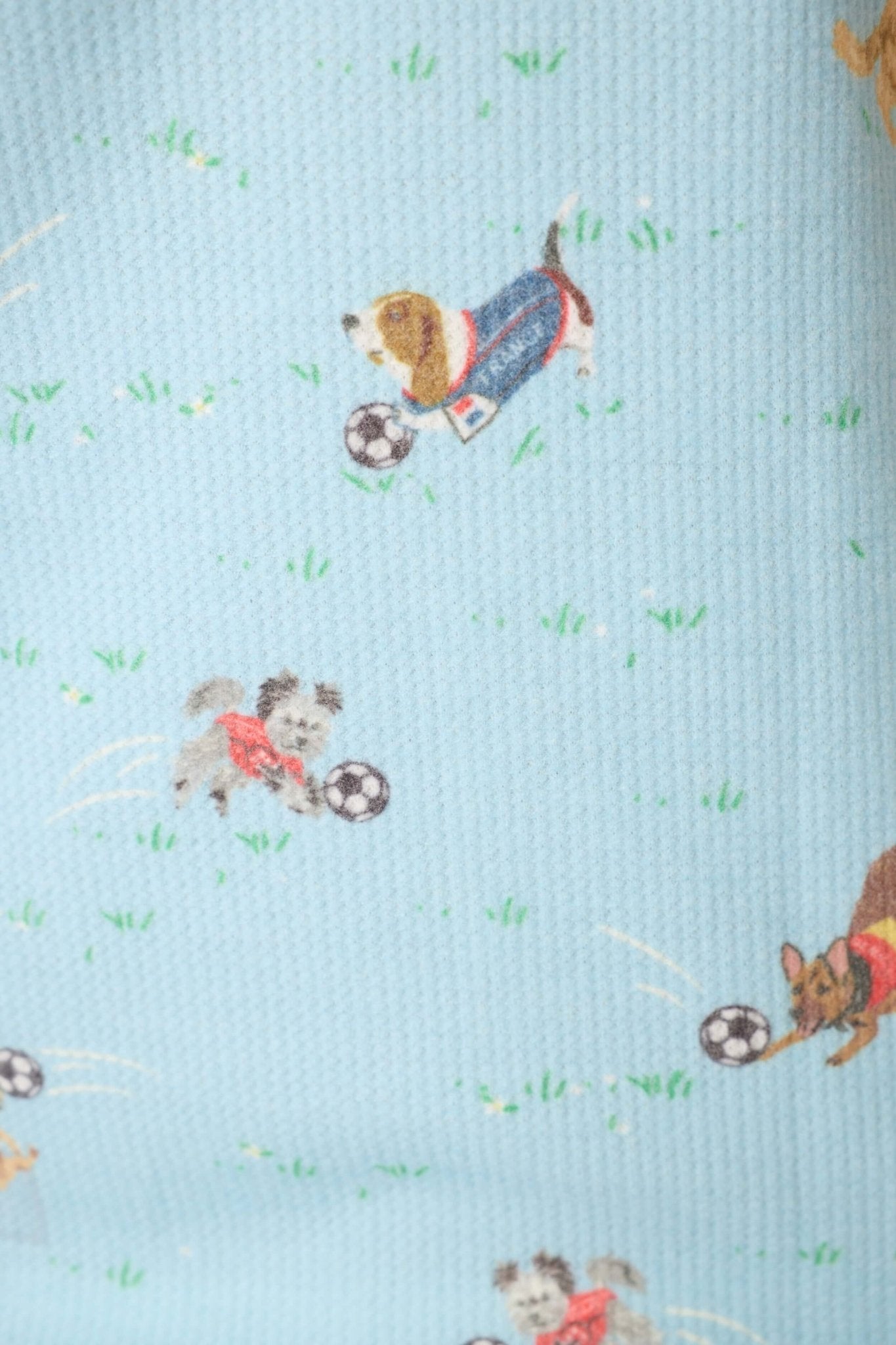Print featuring playful dogs in sports jerseys with soccer balls on a light blue waffle-knit fabric.