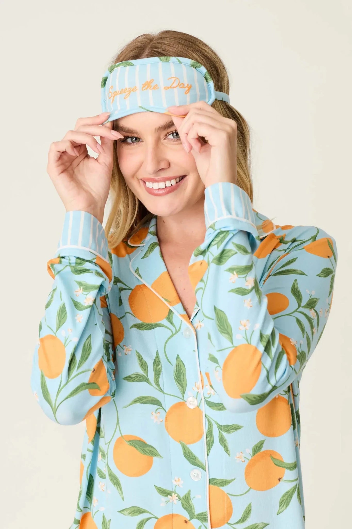Model wearing PJ Salvage Citrus Dreams 3-Piece PJ Set featuring orange design with matching eye mask. Close up view of Eye mask and embroidery saying "Squeeze the Day"
