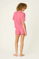 PJ SALVAGE Graphic Print Softee Tee & Short Lounge Set in "Time to Wine Down" rose pink. Model stands against a light background in a back view shot