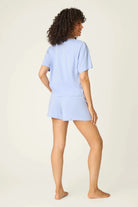 PJ SALVAGE Graphic Print Softee Tee & Short Lounge Set in "Nap Time is my Happy Hour" graphic tee shirt in light blue. Model stands against a light background in a back view shot