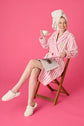 Woman in PJ SALVAGE Playful Cotton Terry Robe enjoying tea while reading on a pink background.