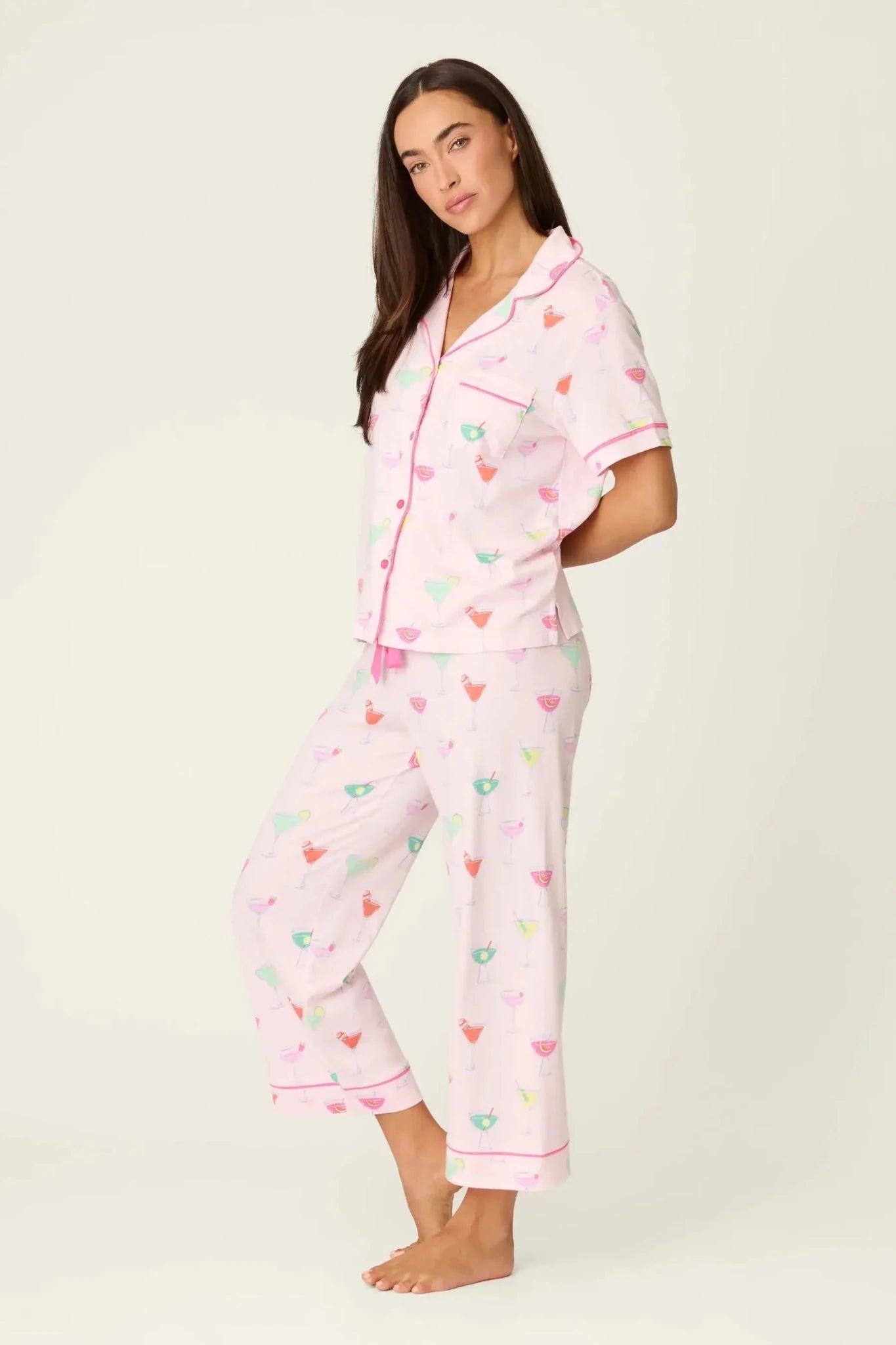 PJ SALVAGE Whimsy Cropped PJ Set in Light Pink Sip Happens print showing cocktail glasses in various colours. Model stands wearing the set against a light background showing the full length in a side profile