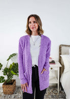 Popcorn Texture Open Summer Cardigan in lilac purple colour shown on model  with jeans and white tee shirt, in a bedroom setting. 