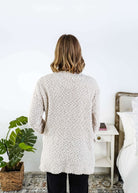 Woman wearing a beige cardigan with texture  in a bedroom setting, Popcorn Texture Open Summer Cardigan showing back of cardigan
