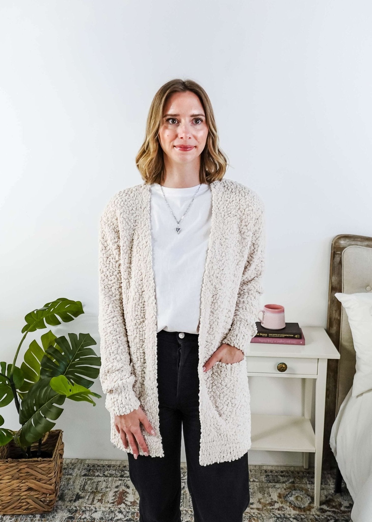 Popcorn Texture Open Summer Cardigan in sand beige, worn by Woman wearing a beige cardigan in a bedroom setting with a white tee and black jeans