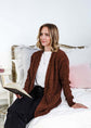 Popcorn Texture Open Summer Cardigan model sits on a bed wearing the rich earthy chocolate brown textured sweater