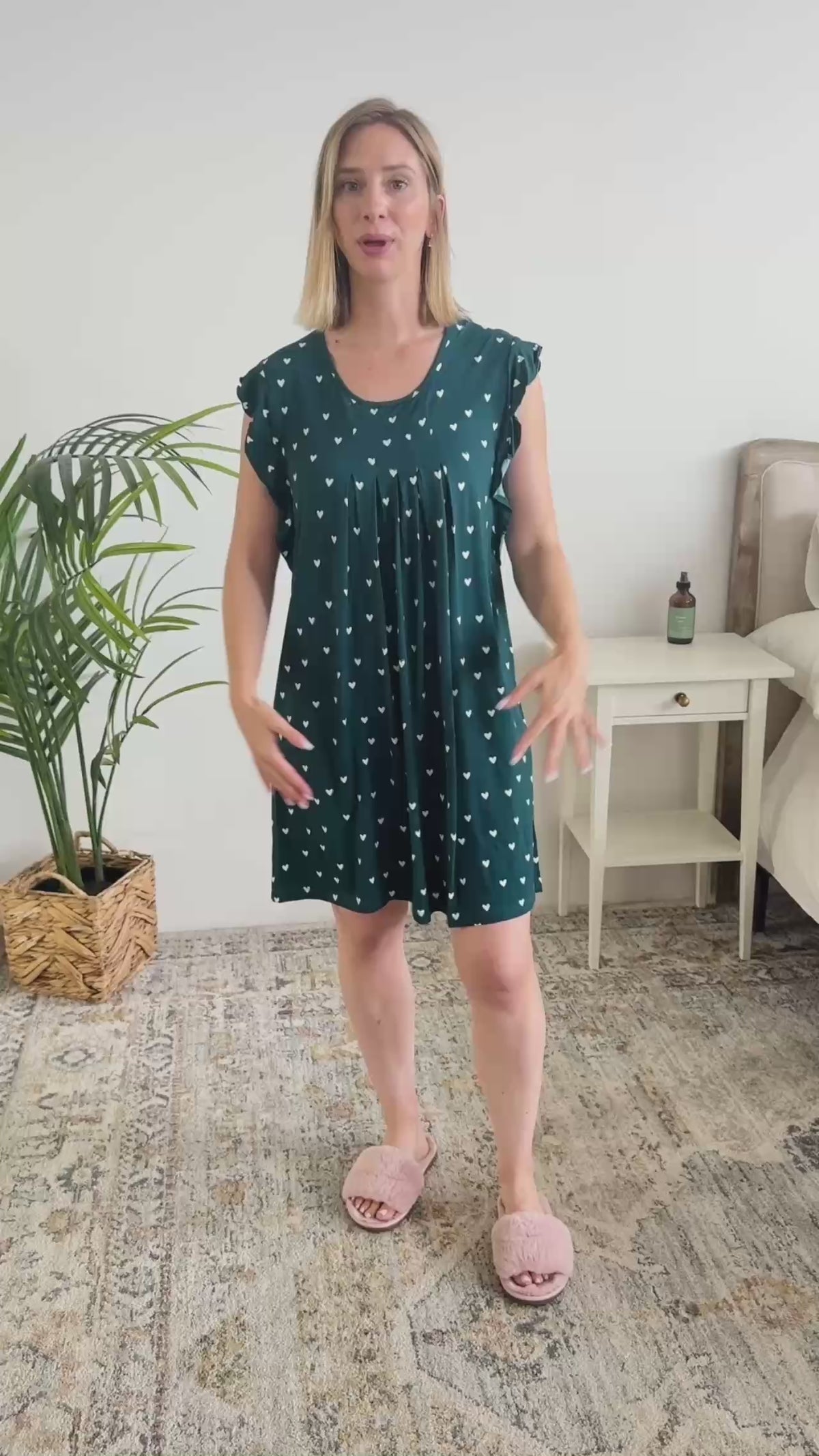Women standing in bedroom showing her nightgown. The night dress is just above the knees with a flowy fit and pleating. The nightgown has little white hearts. 