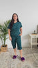 Women turning around in bedroom showing the pajamas she has on. The pajamas are a dark teal colour with hearts and are a capri and t-shirt style. 