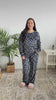 A woman stands and turns around in a bedroom wearing a matching black  pajama with books on it. The set includes a long-sleeve top and matching pants. 