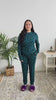 Women standing in bedroom showing her pajamas. The pajamas are a long sleeve top with long pants. The colour is dark teal with cute little white hearts. 