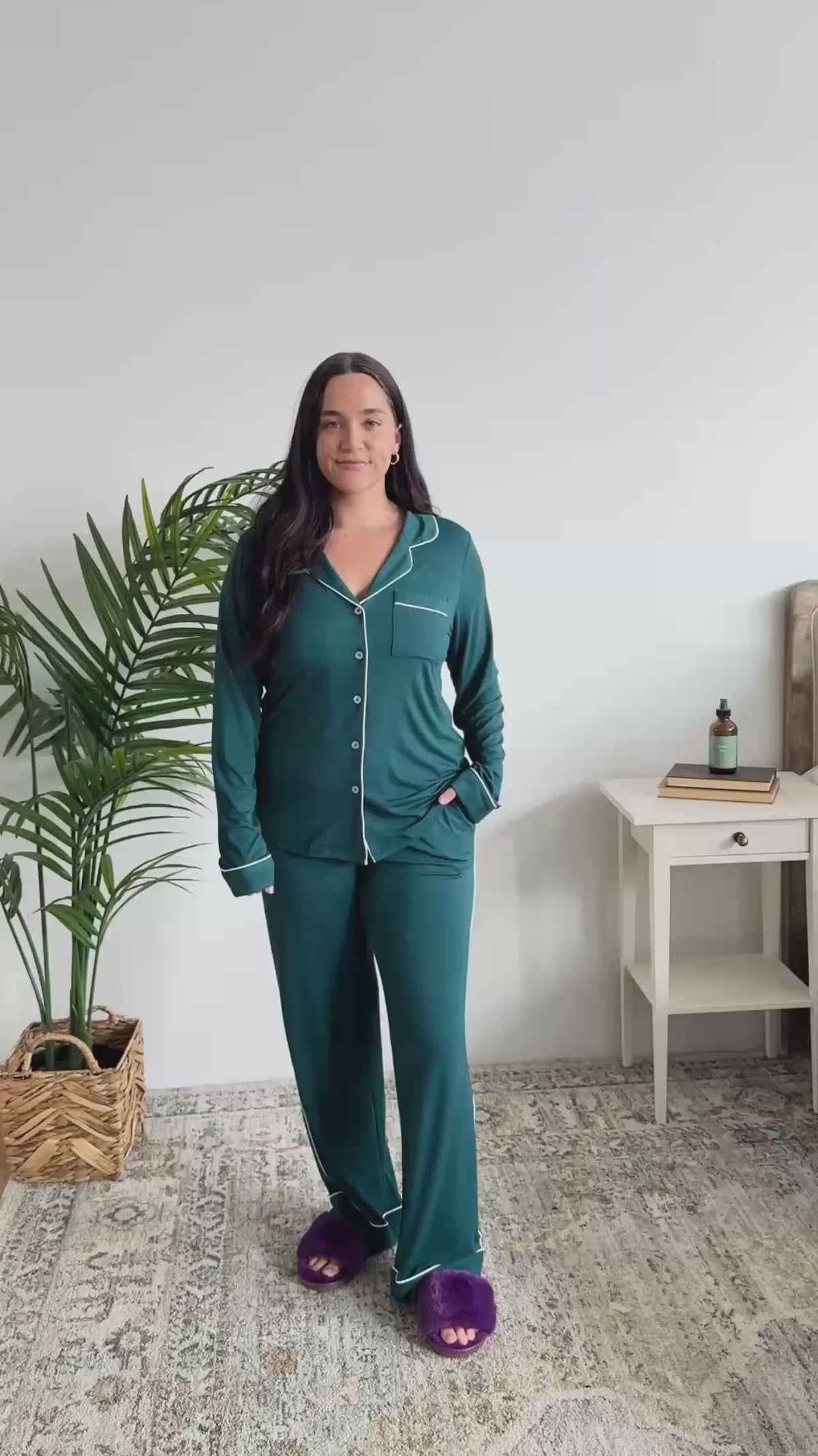 Women standing in a bedroom showing her pajamas. The pajamas are dark teal bamboo pjs with white piping. 