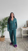 Women standing in a bedroom showing her pajamas. The pajamas are dark teal bamboo pjs with white piping. 