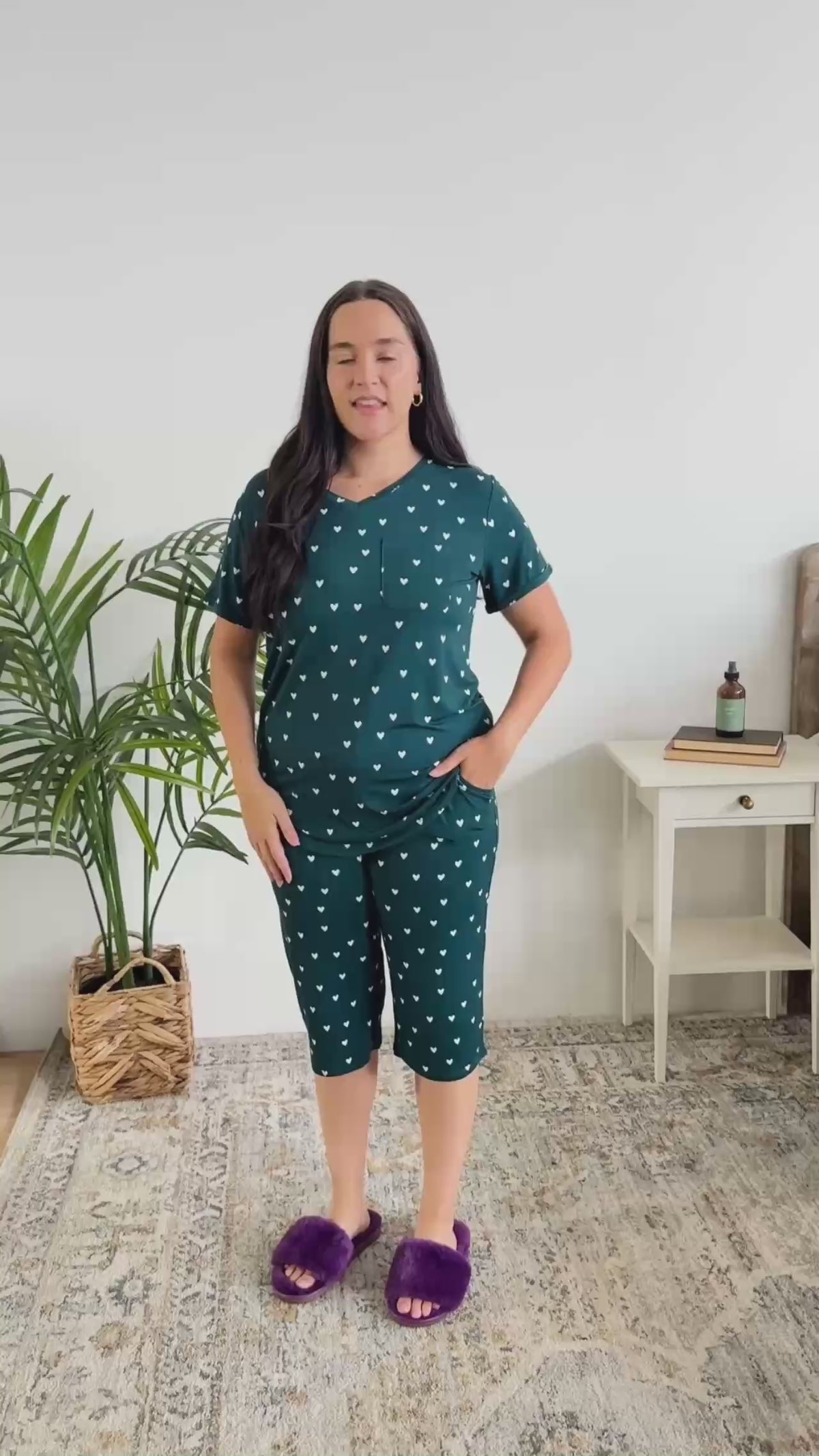 Women standing in bedroom talking about the pajamas she has on. The pajamas are a dark teal colour with hearts and are a capri and t-shirt style. 