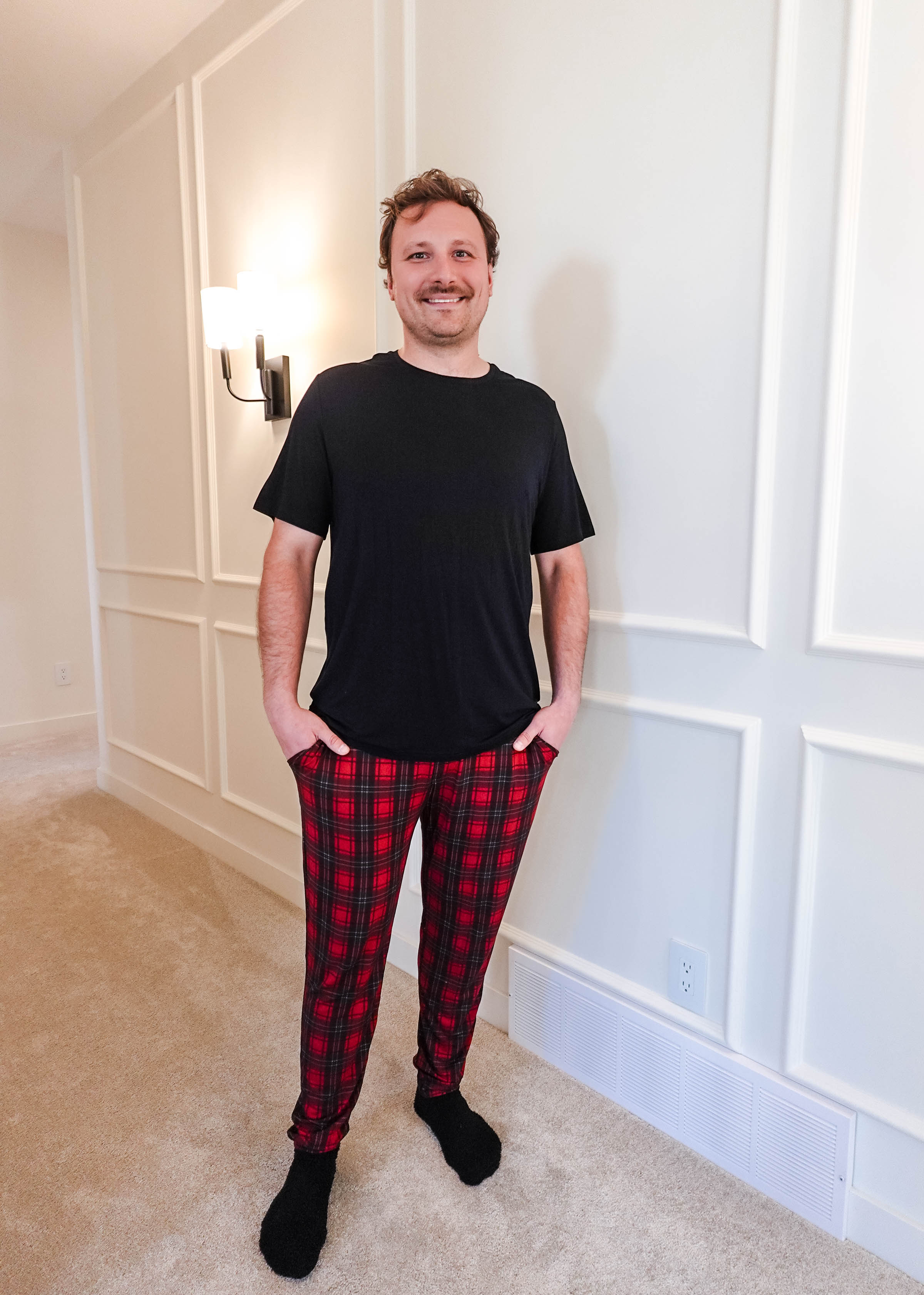 A man wearing a black shirt and Red Plaid Unisex Bamboo Jogger from Bob's Sleepwear Co. standing in a well-lit room.