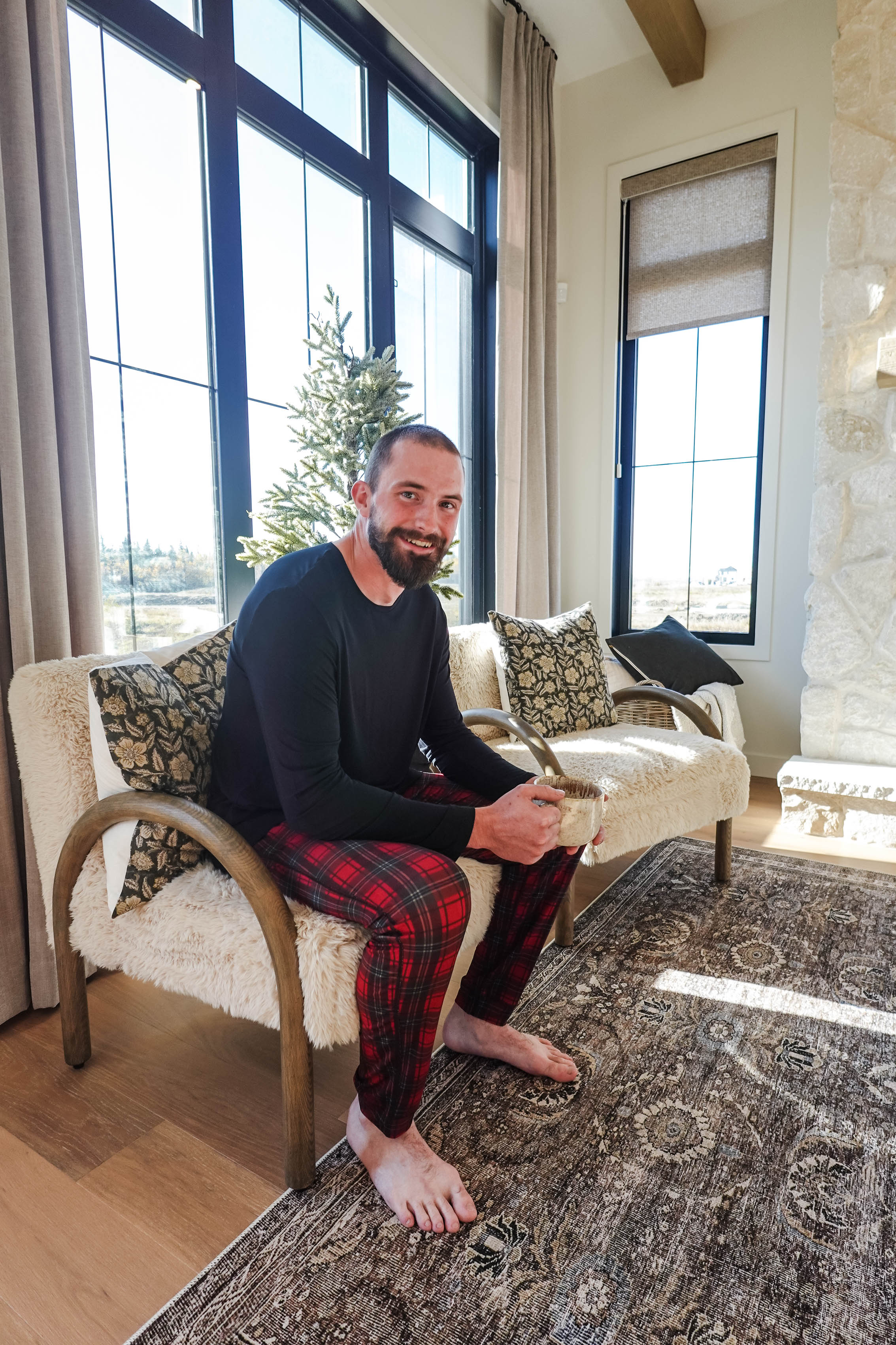 Man sitting in a cozy living room wearing Red Plaid Unisex Bamboo Jogger, enjoying a cup of coffee.