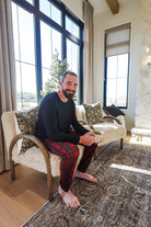 Man sitting in a cozy living room wearing Red Plaid Unisex Bamboo Jogger, enjoying a cup of coffee.