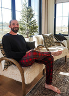 Man sitting on a cozy chair wearing Red Plaid Unisex Bamboo Jogger by Bob's Sleepwear Co.
