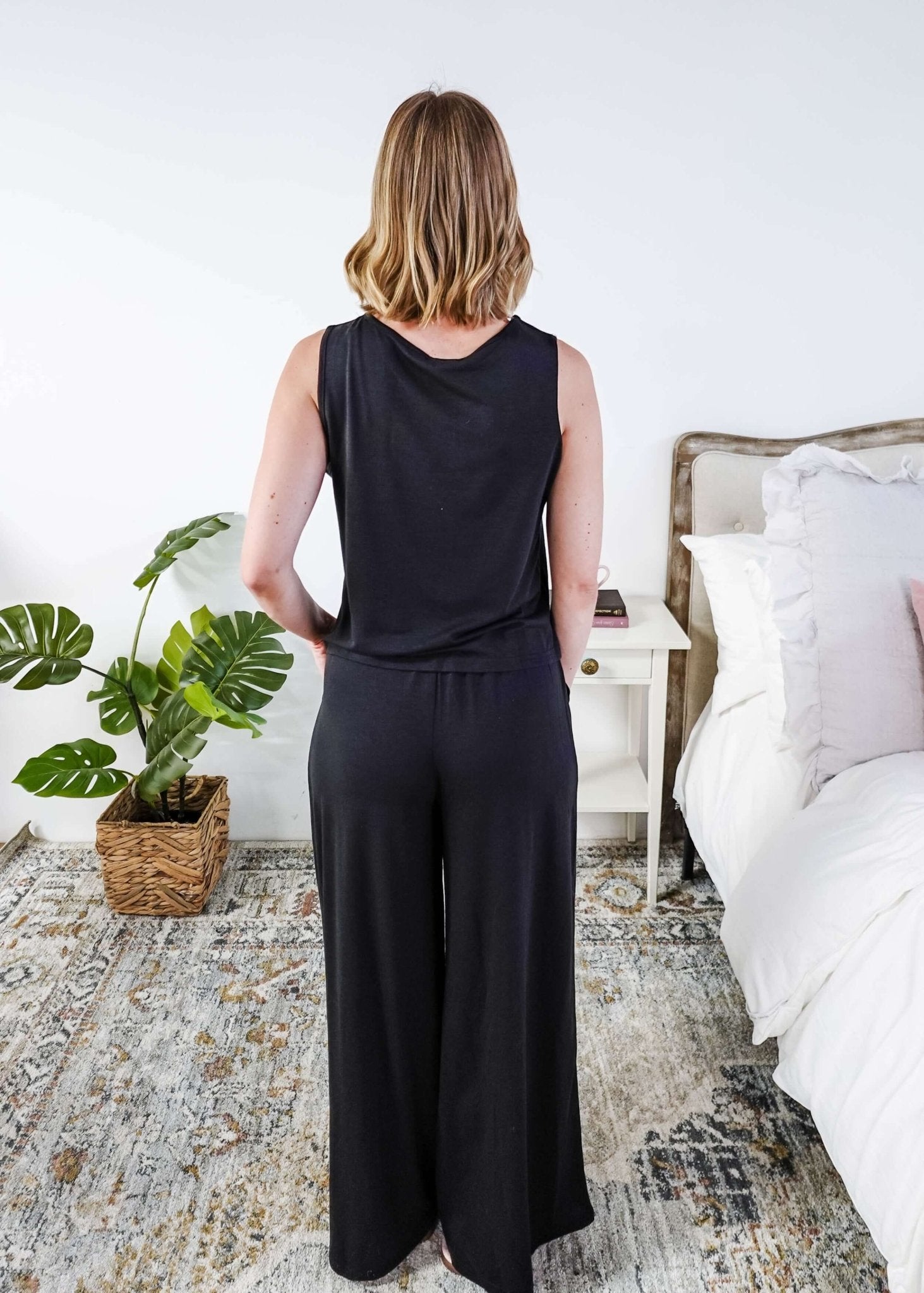 Woman wearing a sleepwear set with a black sleeveless top and pants in a home setting. 