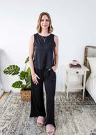 Woman wearing a sleepwear set with a black sleeveless top and pants in a home setting. 