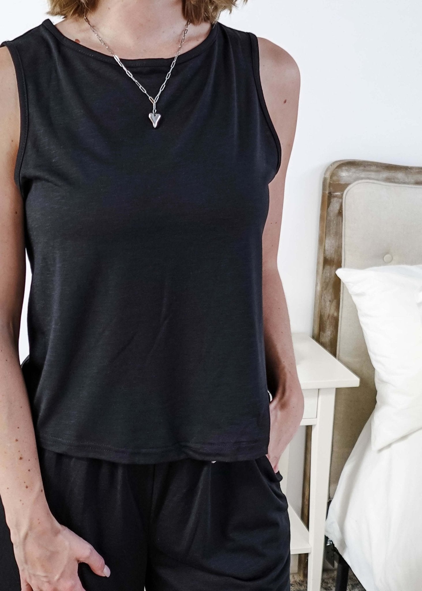 Person wearing a black sleeveless top and black pants in a bedroom setting.