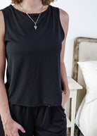 Person wearing a black sleeveless top and black pants in a bedroom setting.