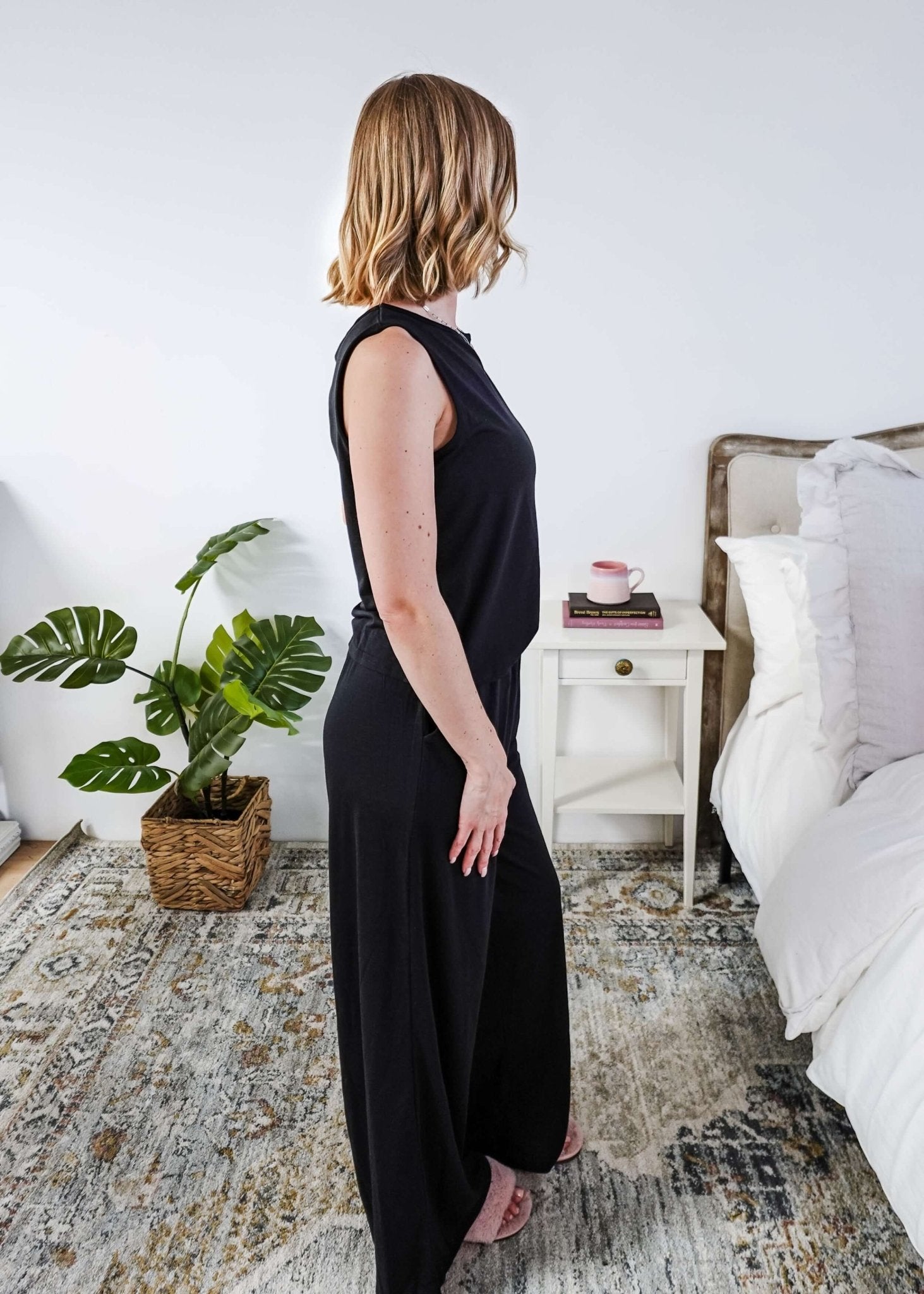 Woman wearing a sleepwear set with a black sleeveless top and pants in a home setting. 