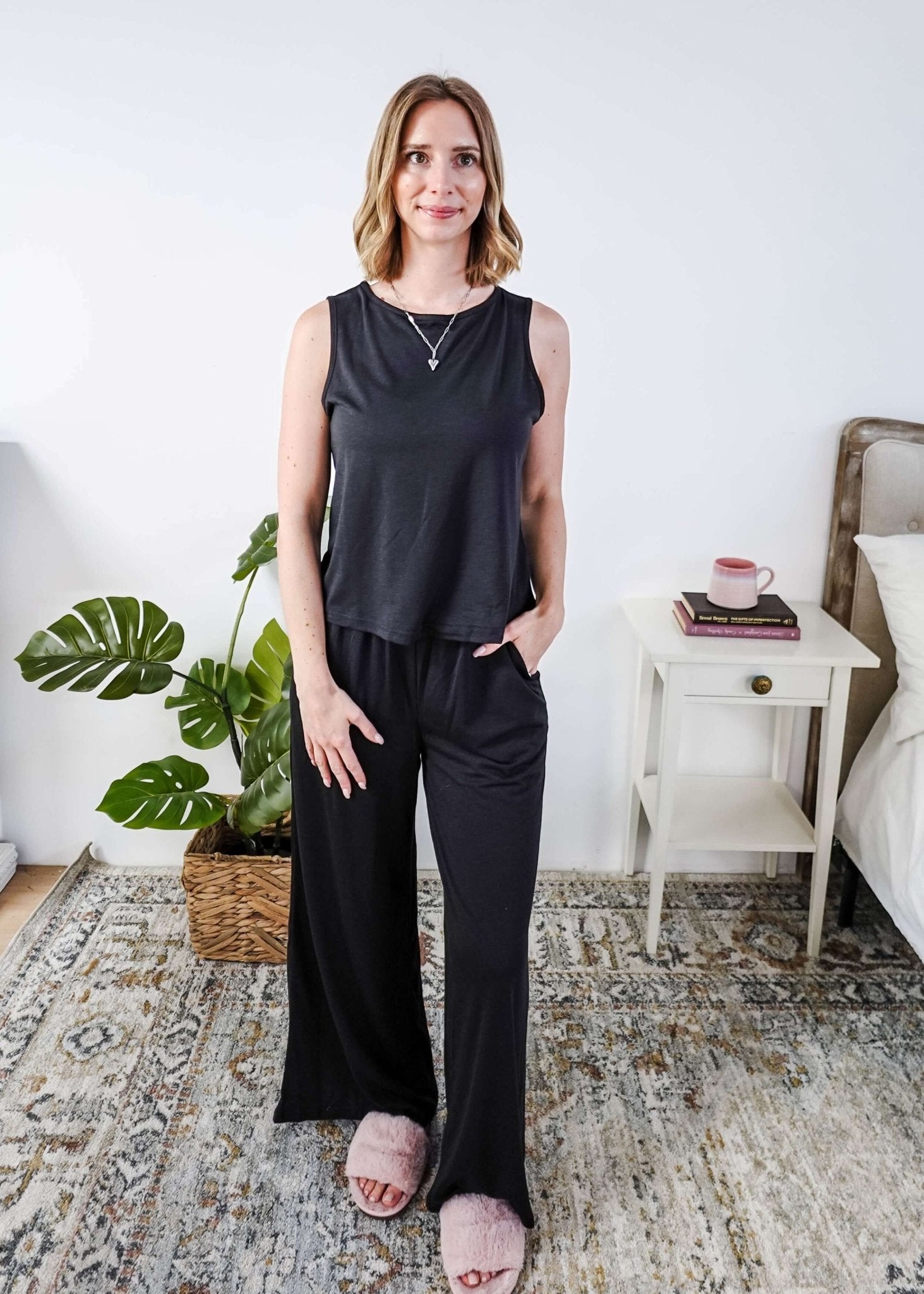 Woman wearing a sleepwear set with a black sleeveless top and pants in a home setting. 