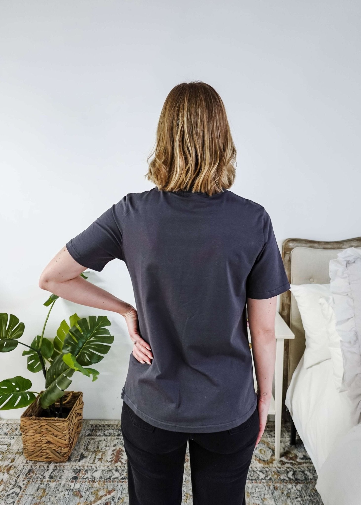 A lady standing in a bedroom in a dark grey shirt. 