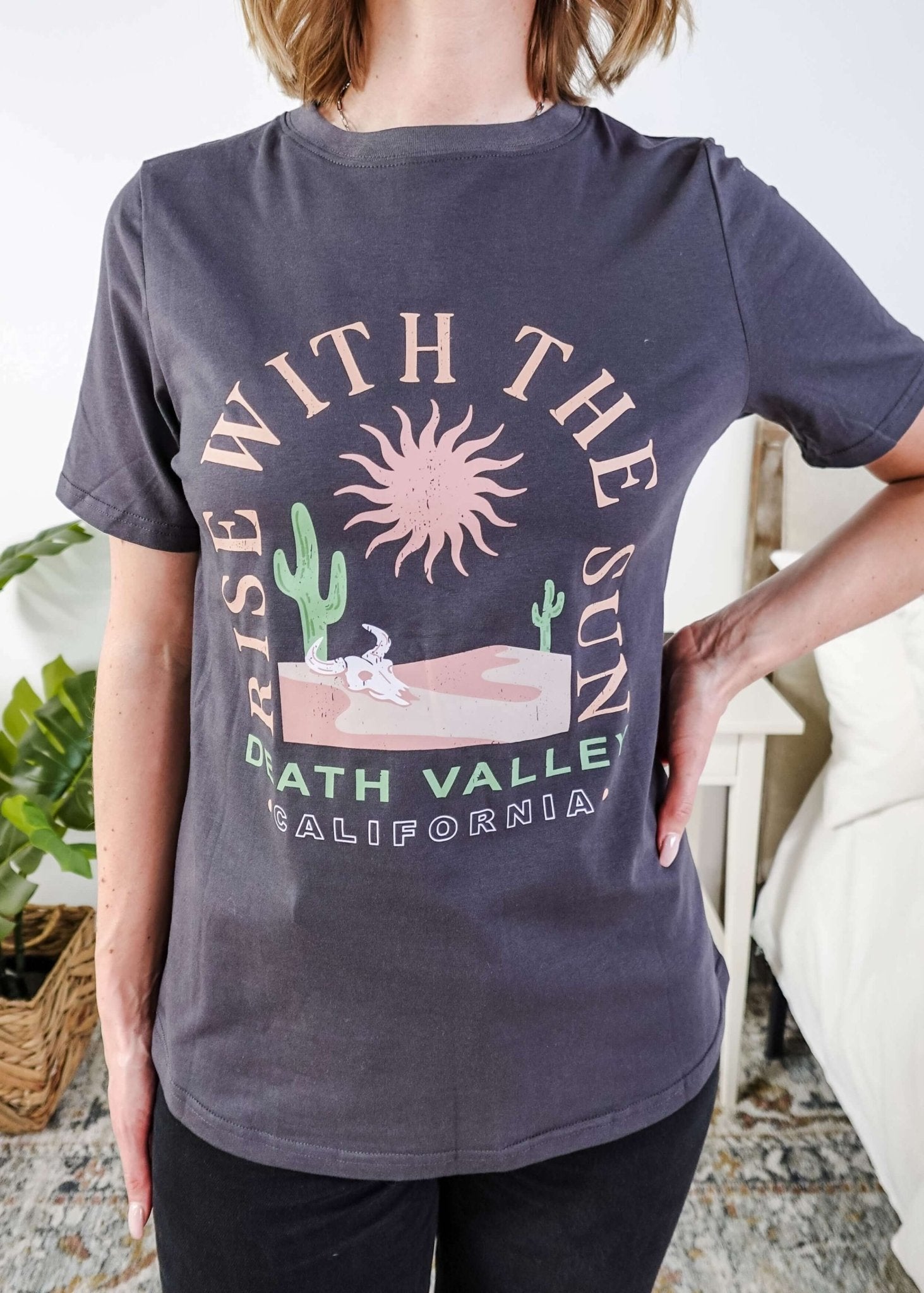 women wearing a dark grey graphic t-shirt with the saying rise with the sun death valley california