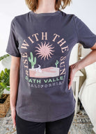 women wearing a dark grey graphic t-shirt with the saying rise with the sun death valley california