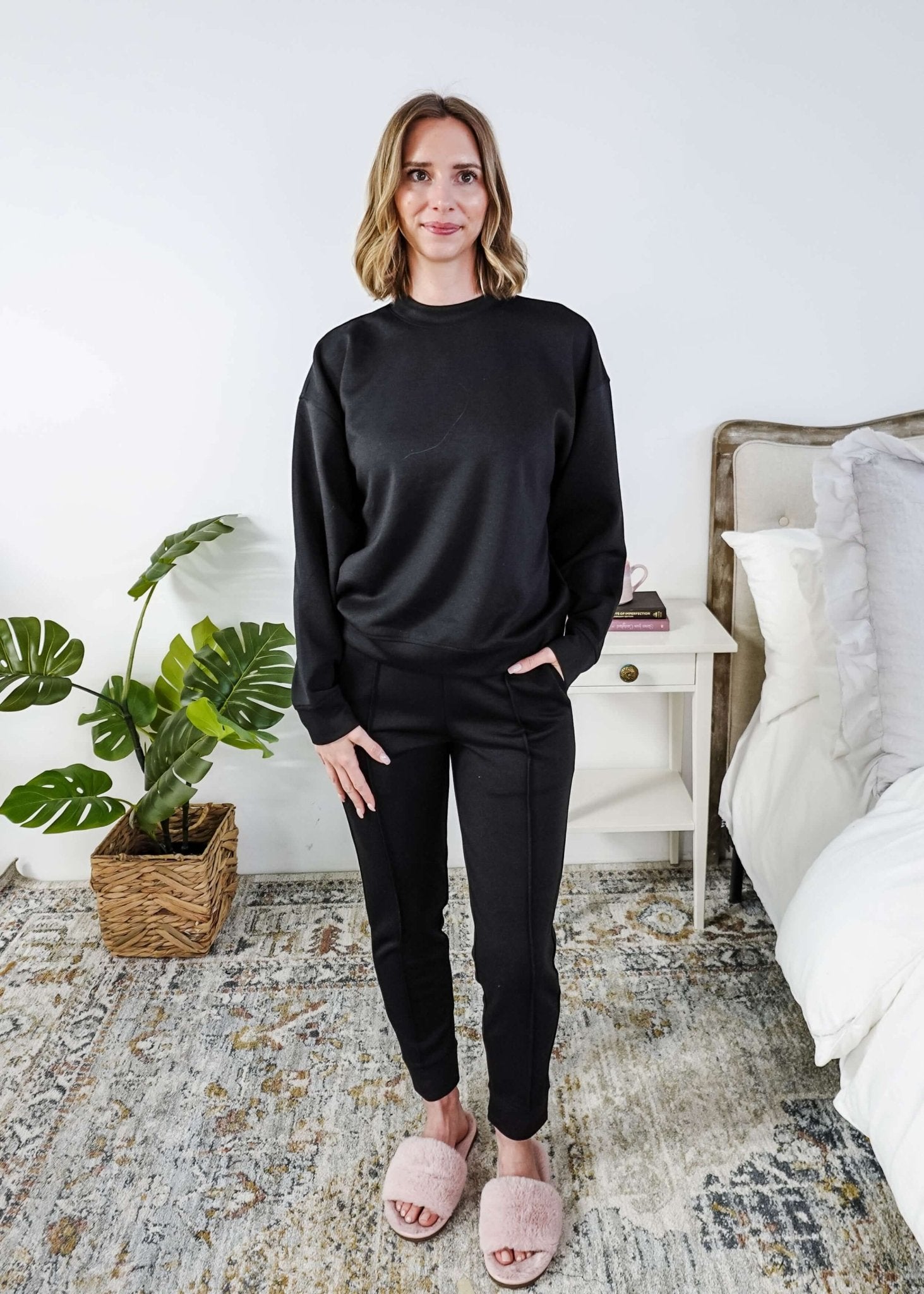 Woman wearing a black lounge  outfit standing in a bedroom.